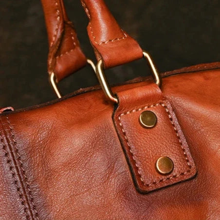 Detailed view of a brown leather bag clasp, highlighting the buttons and quality stitching.