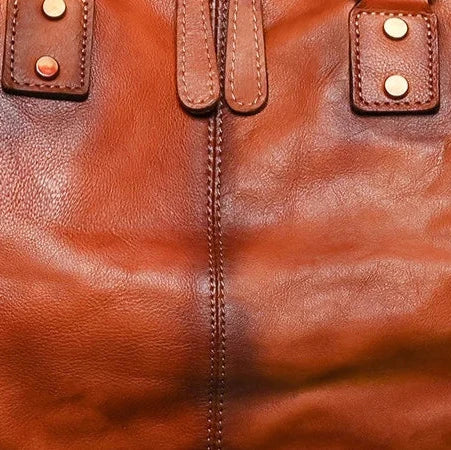 Detail of a brown leather bag, showing the metal buttons and refined leather texture.