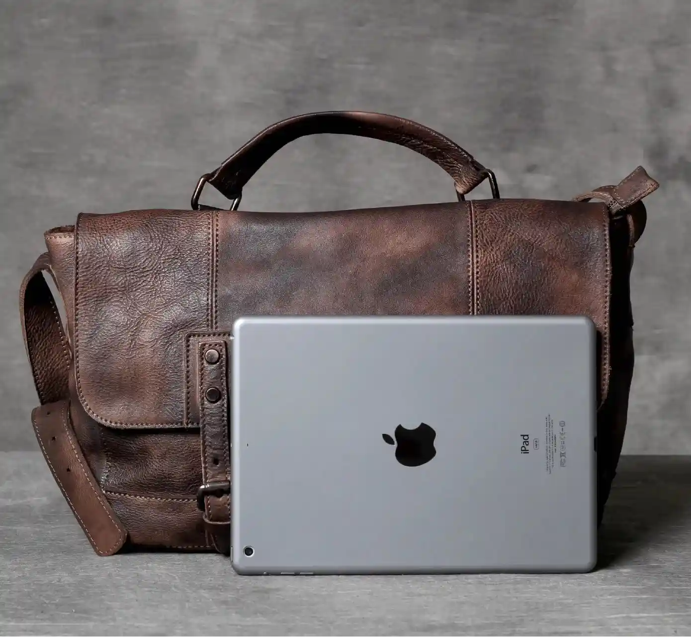 A brown leather bag with an iPad tablet for size reference, front view.