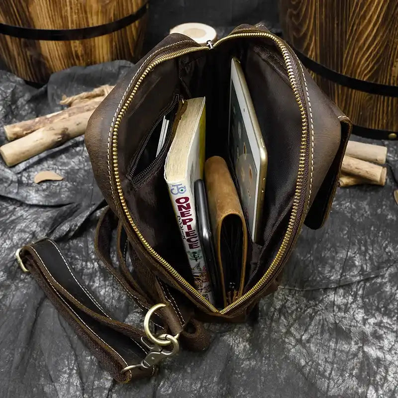 open brown leather bag, showing various items inside, such as a book, a tablet and a wallet.