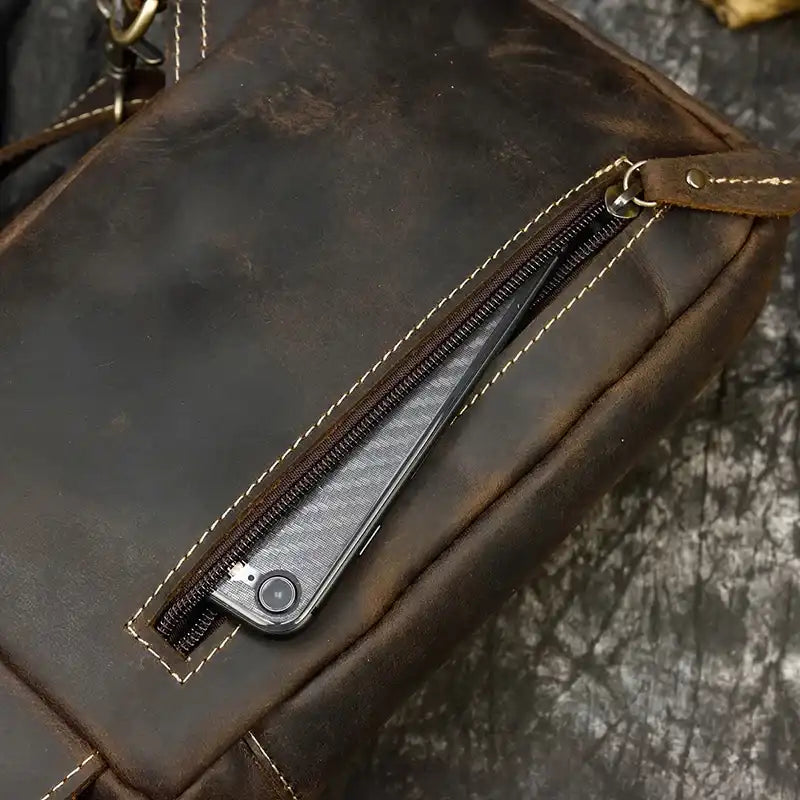 A brown leather bag with an open zipper, revealing a smartphone inside.