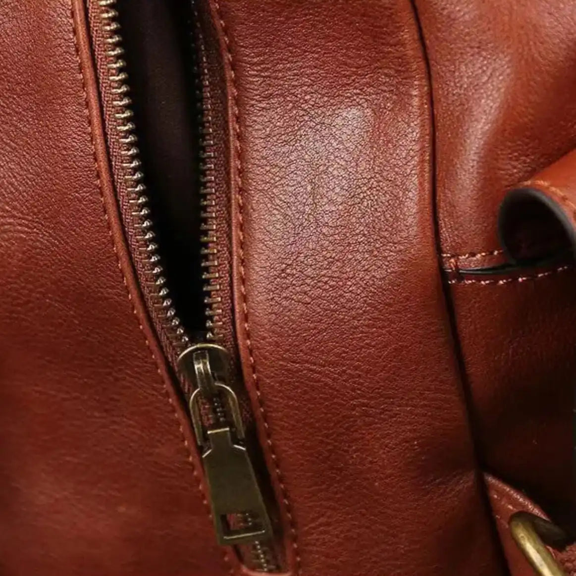 Detailed image of a zipper on a brown leather material, highlighting the texture and quality of the finish. 
