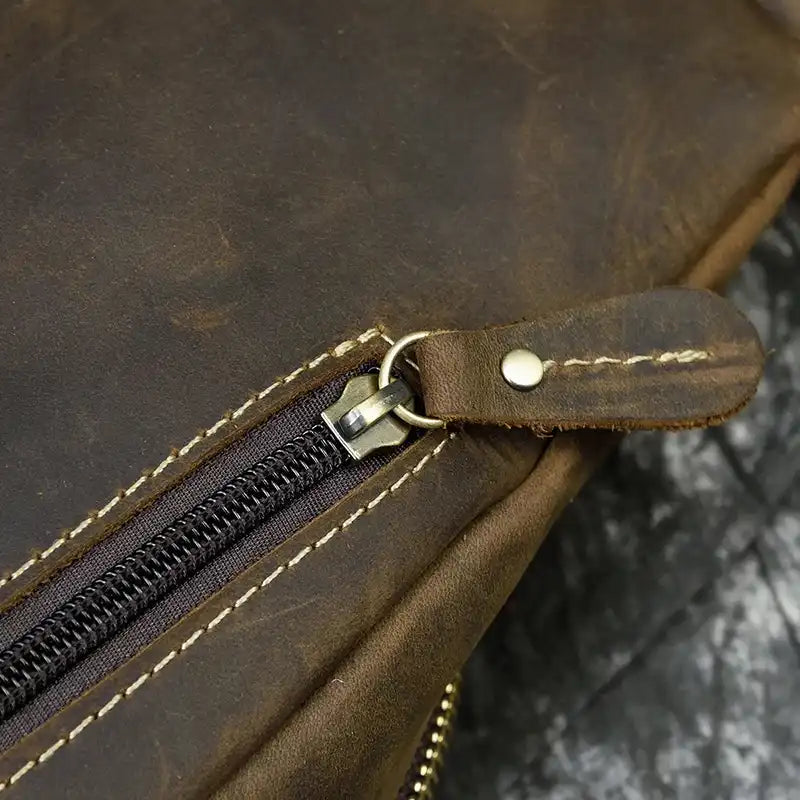 Detail of a zipper on a brown leather bag, highlighting the stitching and handcrafted finish.