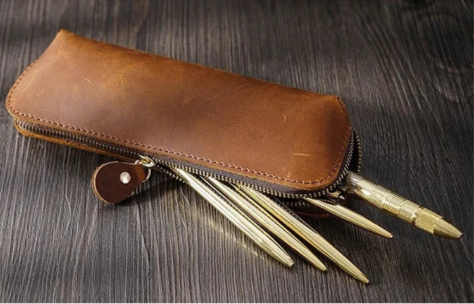 open sophisticated brown leather pen case with gold pens sticking out.