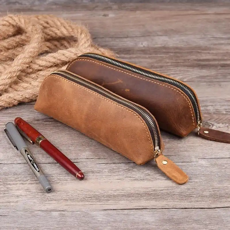 Set of brown leather cases with  zipper next to pens on a rustic wooden surface. 
