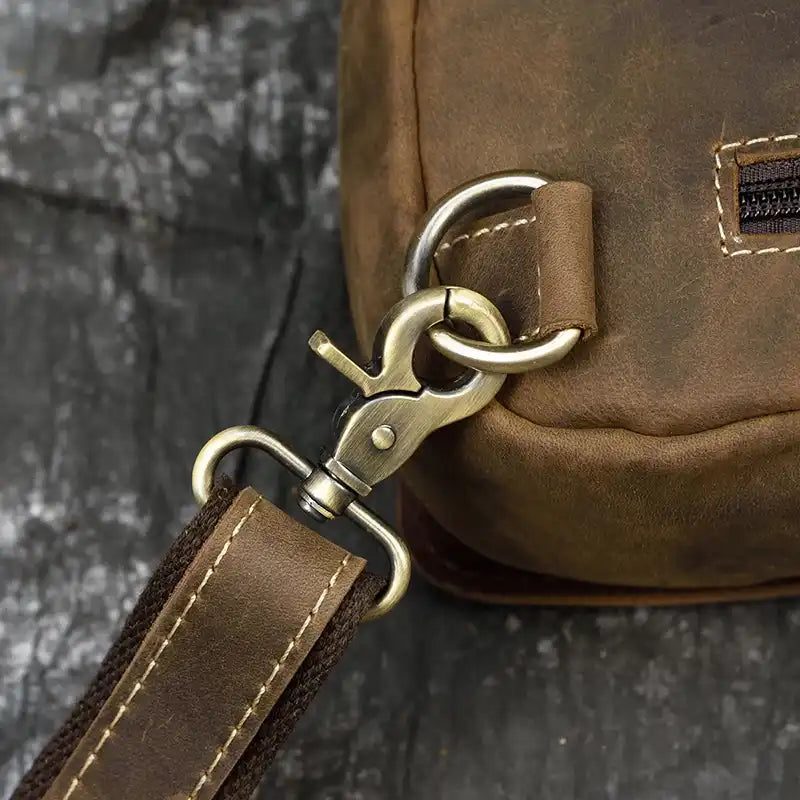 Detail of a metal clasp on a brown leather bag, showing high quality stitching and material.