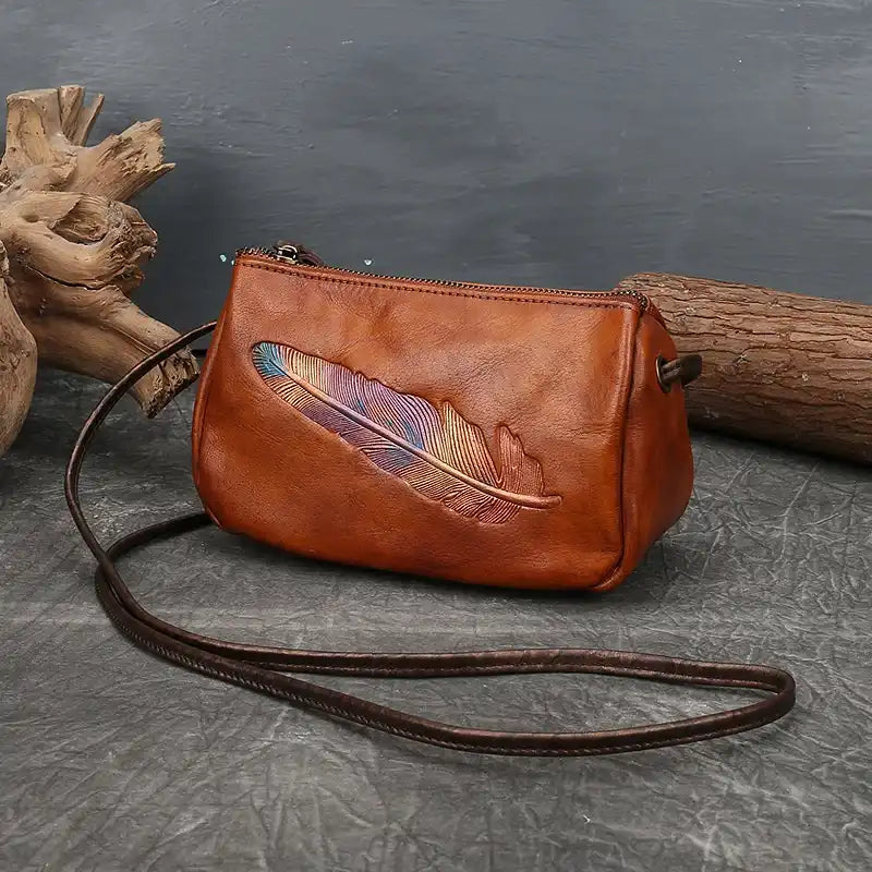 Brown leather crossbody bag with colorful feather detail, ideal for those who appreciate unique and elegant accessories.