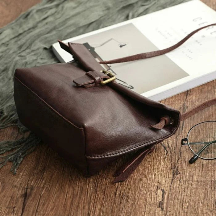 bottom view of a brown leather crossbody bag showing with front buckle and adjustable strap.