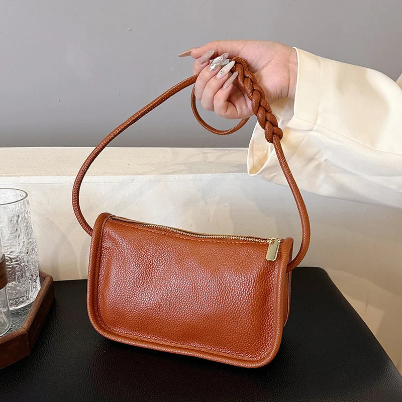 A stylish brown crossbody bag with a braided strap, held by a person.