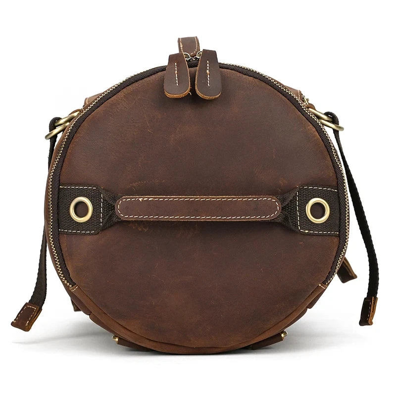 Round shaped brown leather duffle bag. Elegant and functional design, with handles and zipper closure, top view.