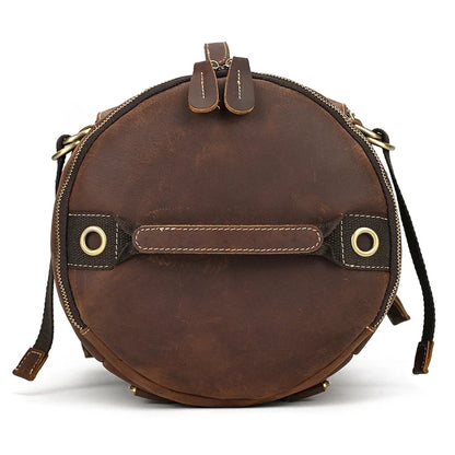 Round shaped brown leather duffle bag. Elegant and functional design, with handles and zipper closure, top view.