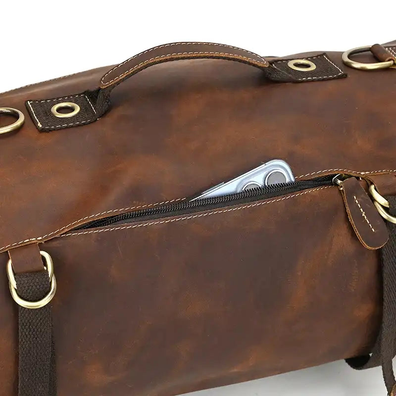 Brown leather duffle bag with front pocket and visible phone, ideal for everyday use and travel. 