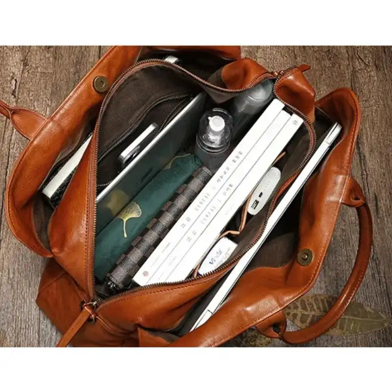 View of an open brown leather bag showing several organized items, such as books, a notebook and a bottle.