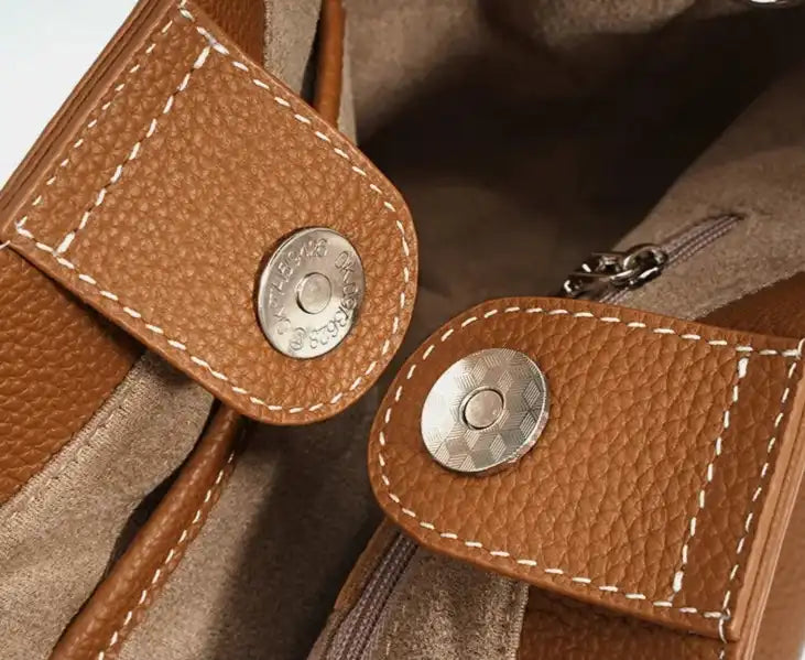 Detail of a brown leather pocket clasp, highlighting the texture and elegant metal buttons.