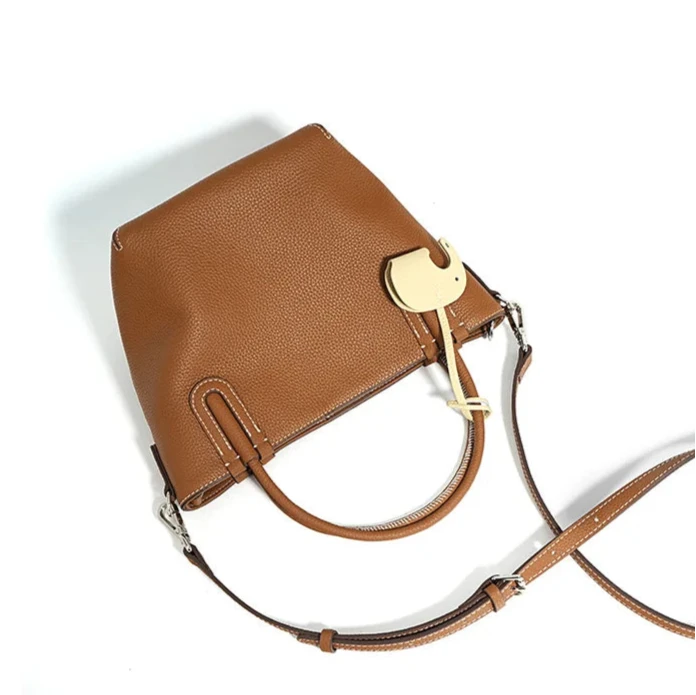 A stylish brown handbag with a unique elephant charm and adjustable strap.