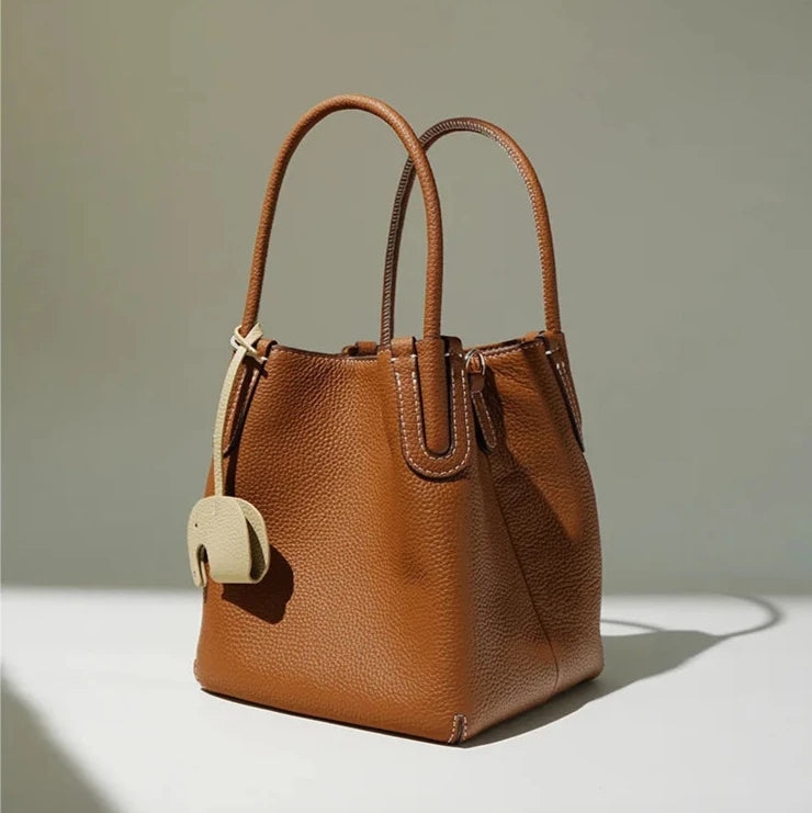 Modern brown leather handbag with elegant handles and elephant charm.