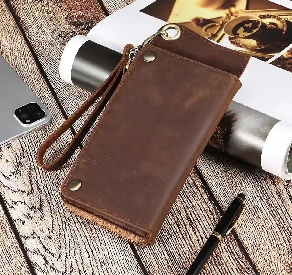 Brown leather wallet on a wooden table with phone and pen - top view.