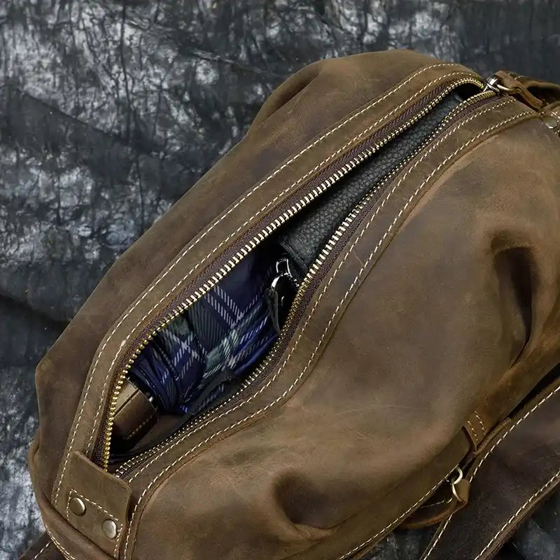 Detail of a brown leather bag with open zipper, showing the interior with items inside, showcasing large capacity.