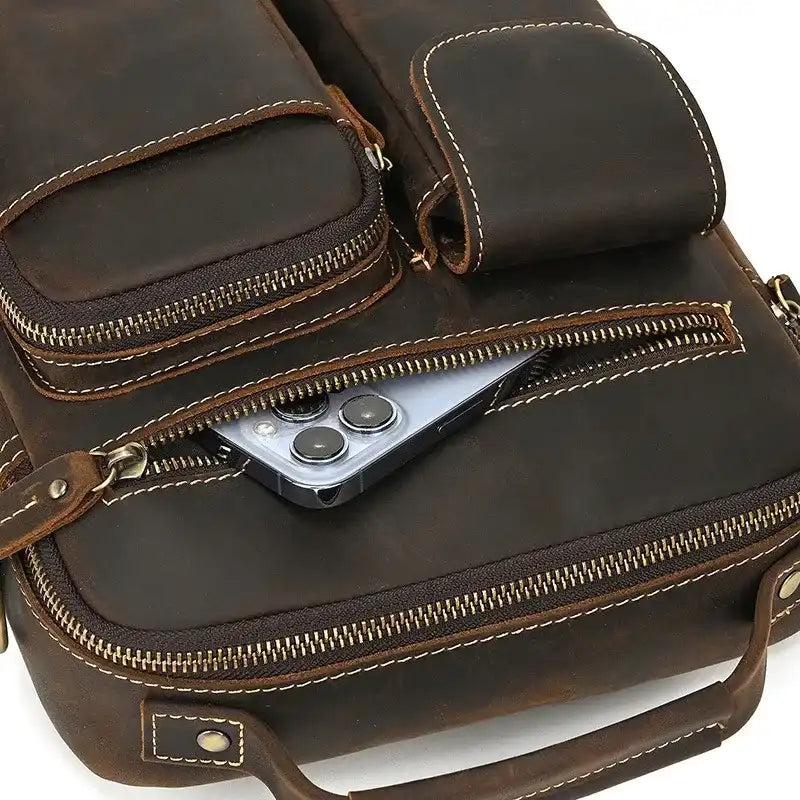 A brown leather briefcase with multiple compartments and a smartphone visible on one of the zip pocket.