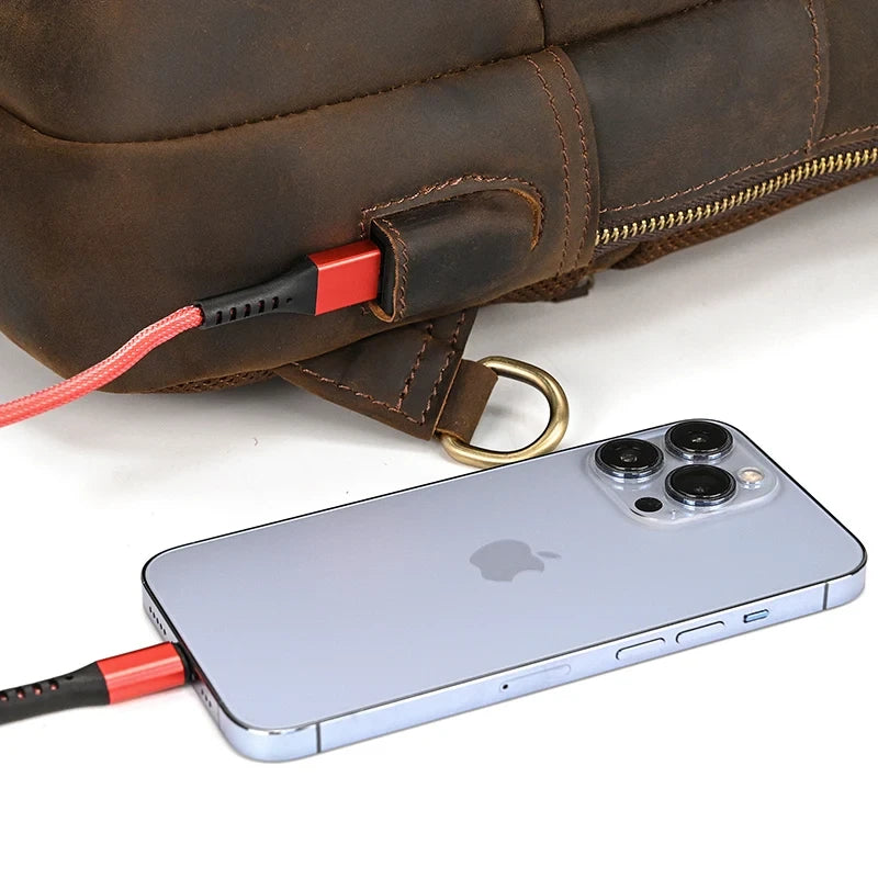 smartphone connected to a charging cable in a leather bag demonstrating the bag's technological feature.