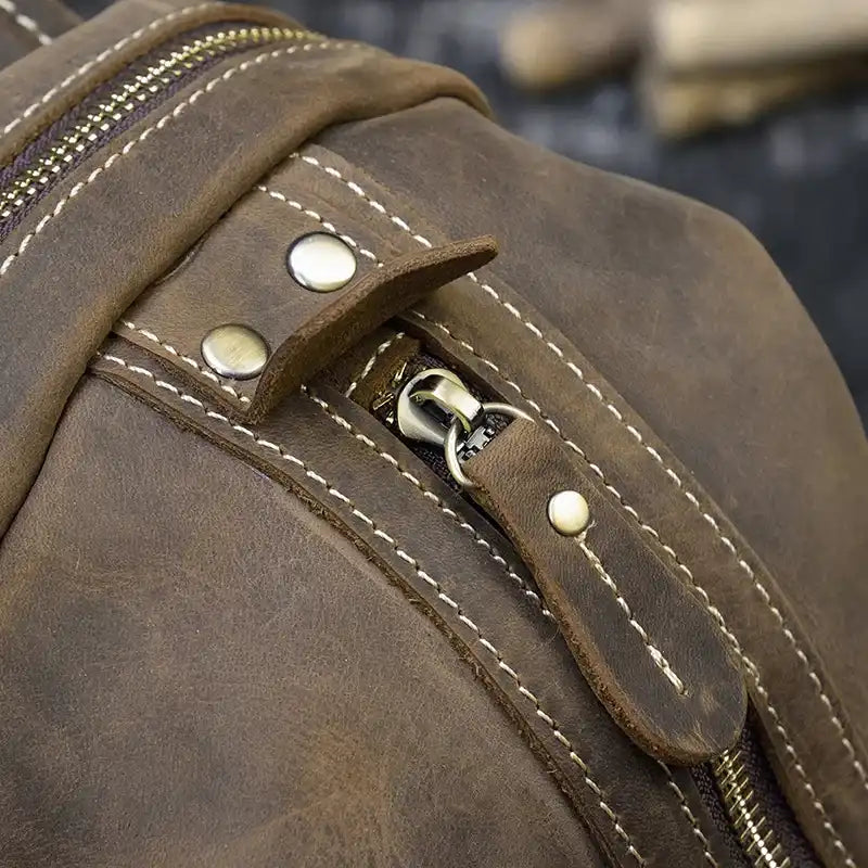 Detailed view of a zipper on a brown leather backpack, highlighting the stitching and metal buttons.