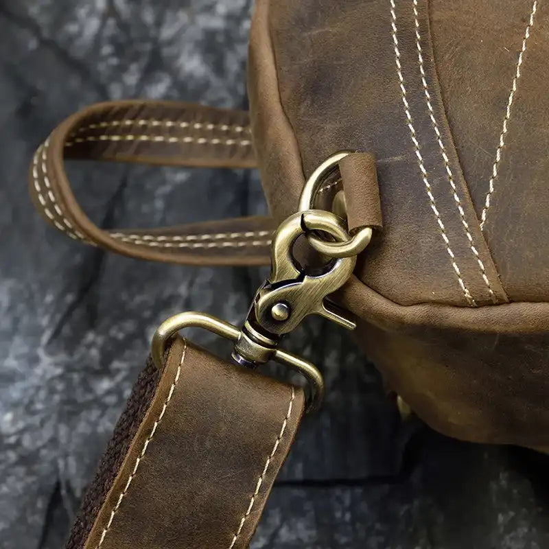 Detail of a brown leather bag clasp, showing the metal support and stitched finish.