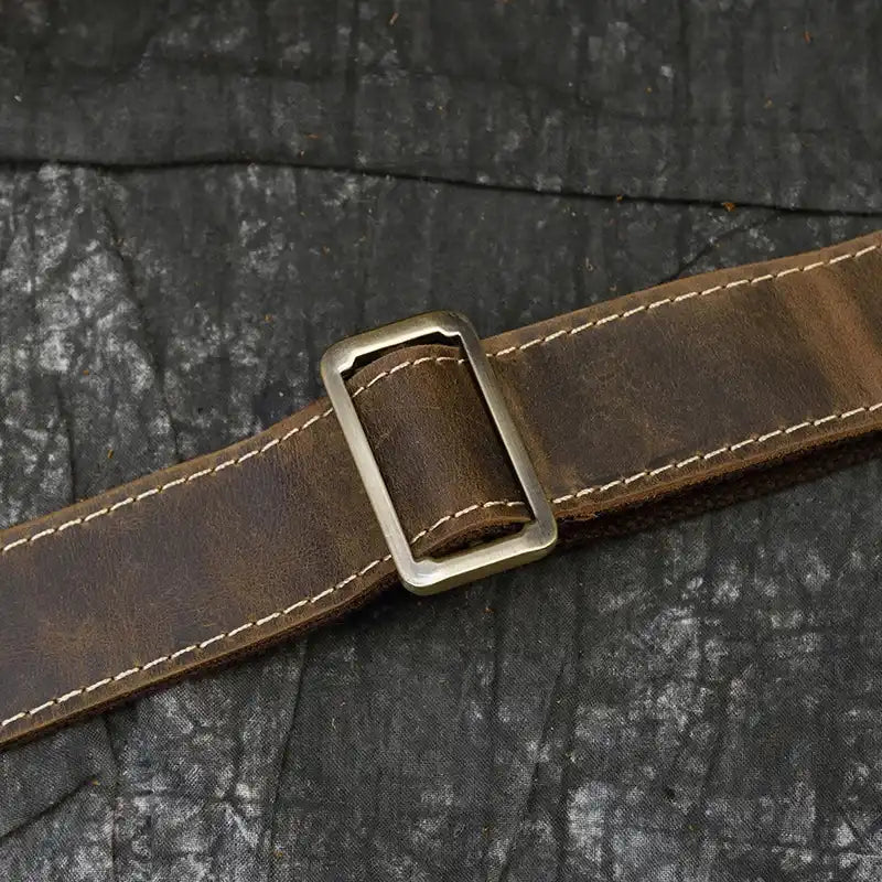 Brown leather bag belt with metal buckle on a textured background.