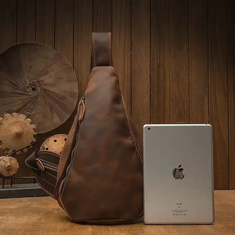 brown leather sling bag displayed with an iPad for size comparison.