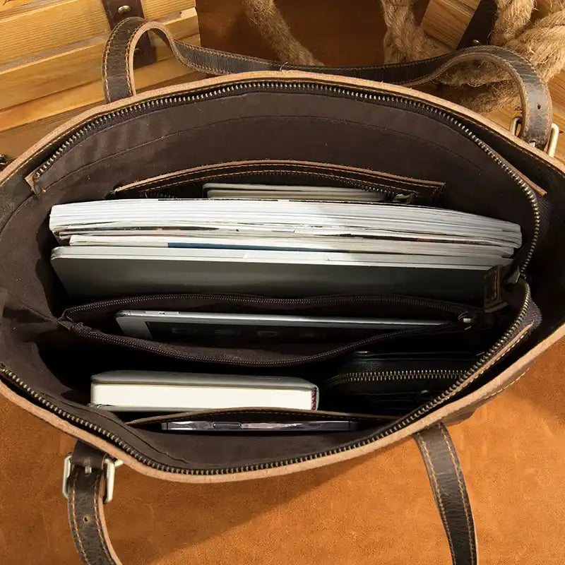 Inside view of a stylish brown leather tote bag with notebooks, a laptop, and magazines organized.