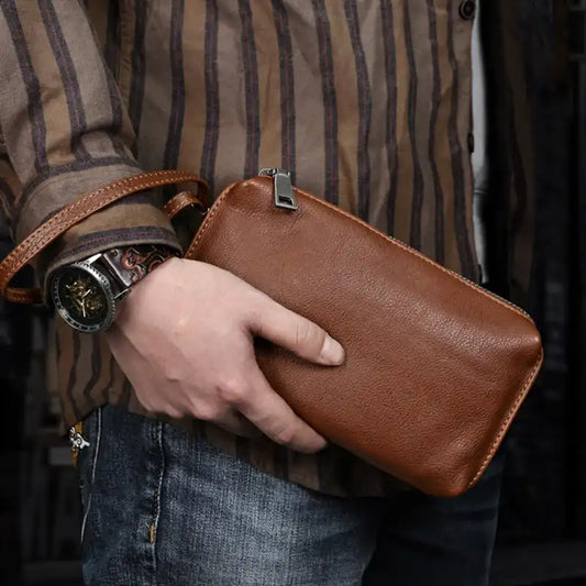 A stylish brown leather wallet held by person by wrist strap. 
