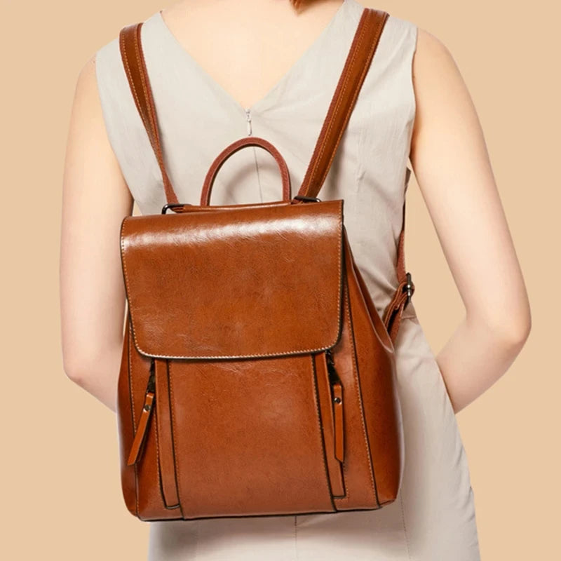 A stylish brown leather backpack worn on the back of a woman.