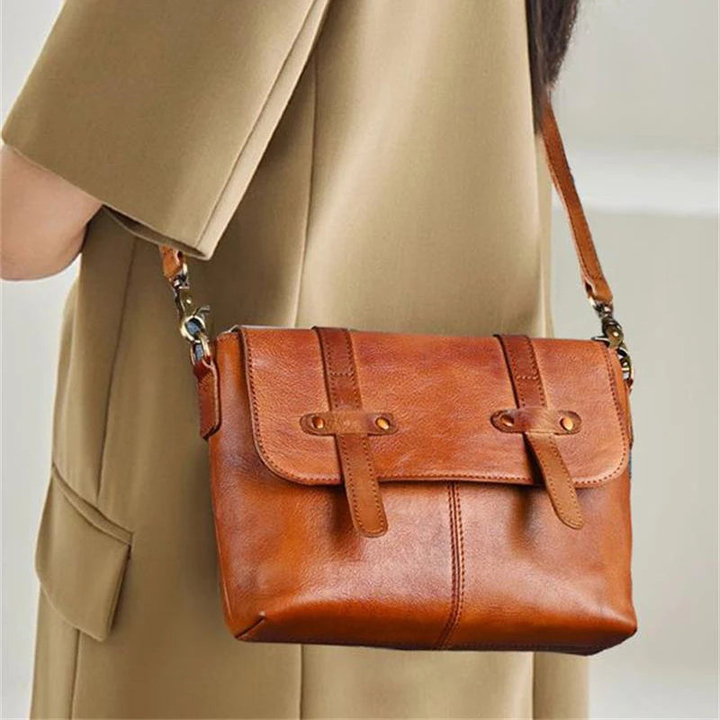 A stylish brown leather shoulder bag with a flap and strap worn over the shoulder by a woman.