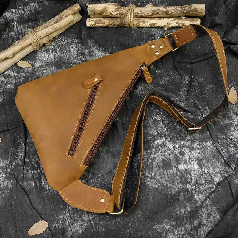 Close-up view of a brown leather sling bag highlighting its zippers and strap details.
