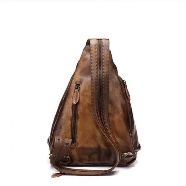 back view of a triangular shaped brown leather shoulder bag with multiple zippers and a unique strap design.