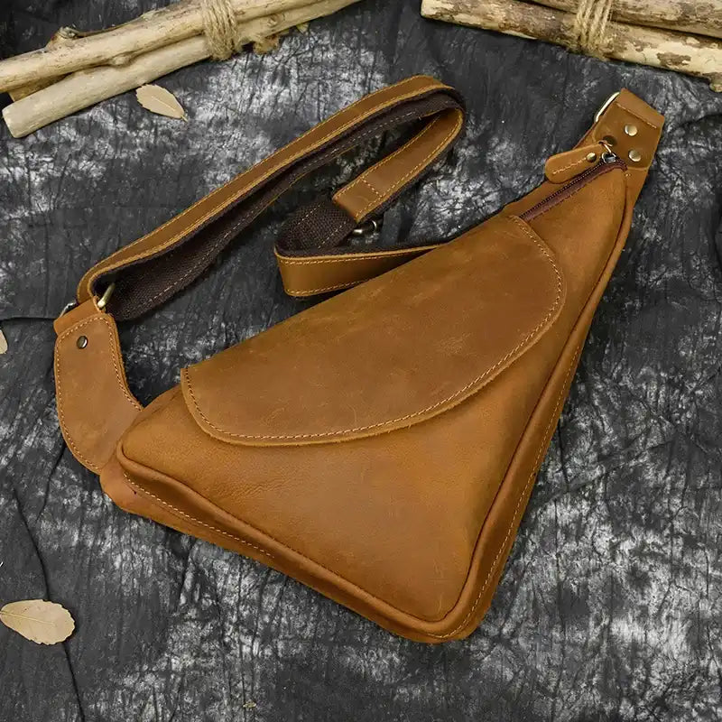 Unique brown triangular leather sling bag with adjustable strap and flap closure.