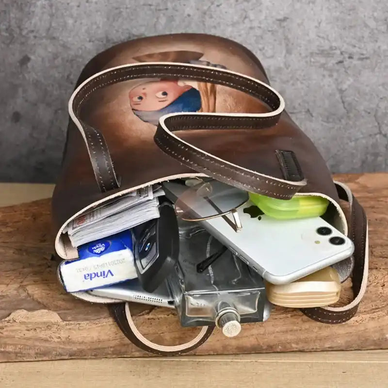 A brown leather tote bag filled with personal items, including a cell phone, books, glasses, and other accessories.