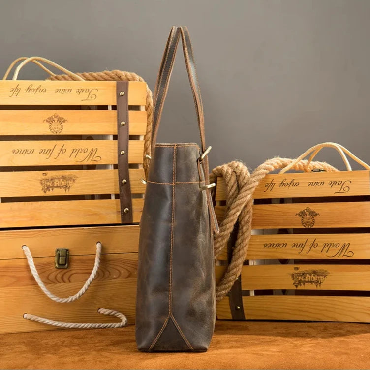 A vintage leather tote bag showcased with rustic wooden crates and rope - side view.