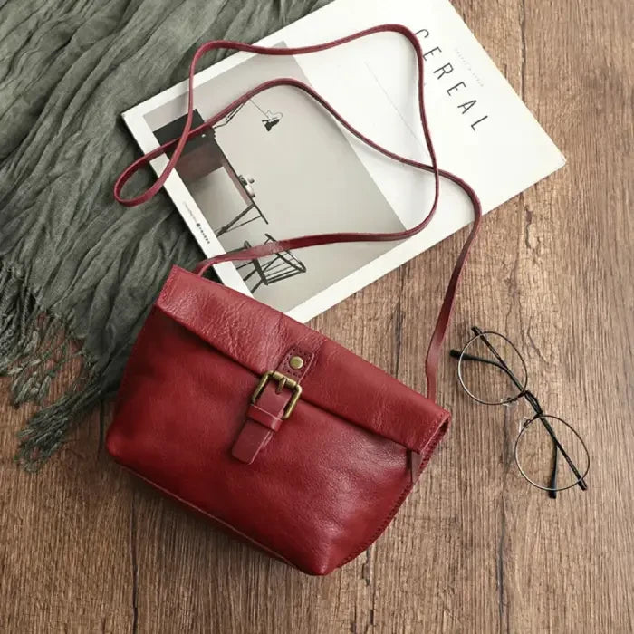 Burgundy leather crossbody bag with elegant buckle and long strap, top view.