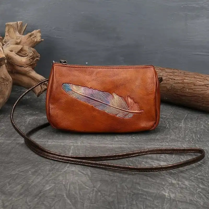 Brown leather crossbody bag with colorful feather embossed detail, front view.