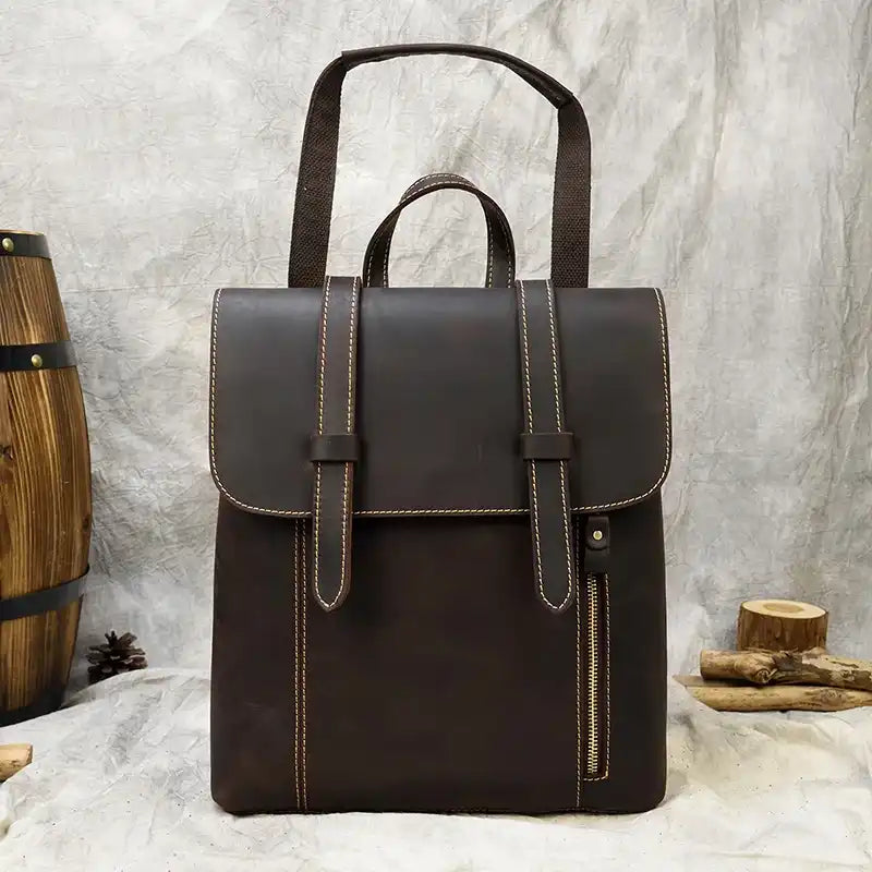 Coffee brown leather backpack with light stitching details, front zipper, soft handle and adjustable strap, front view.