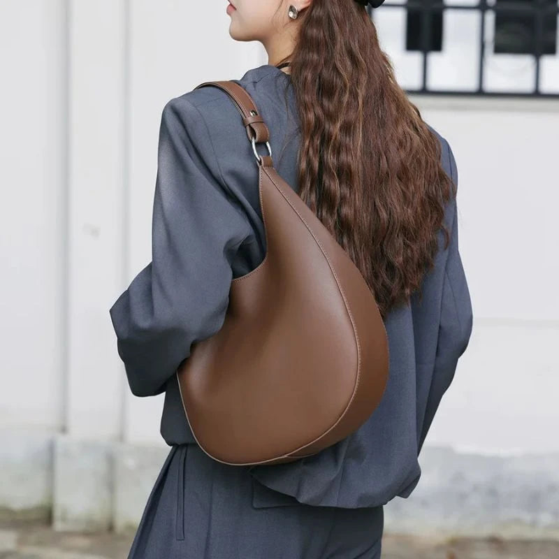 Model wearing a coffee brown leather bag on her shoulder.