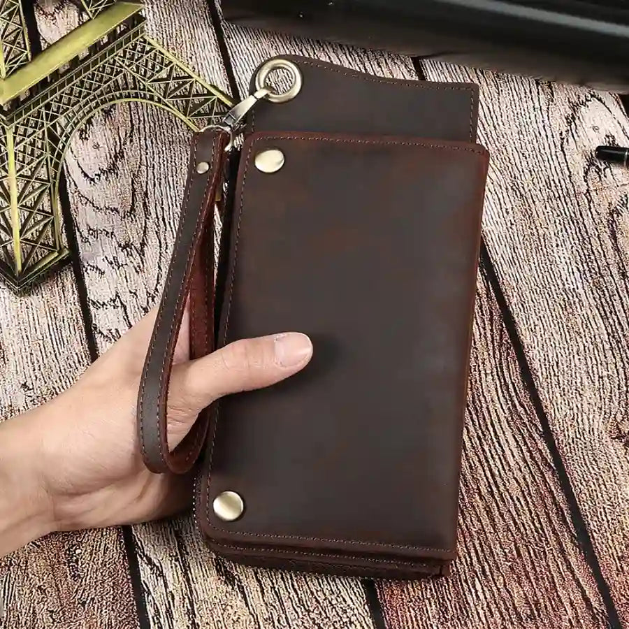  a dark brown leather wallet with wrist strap being held by a hand, highlighting its elegant design and functionality.