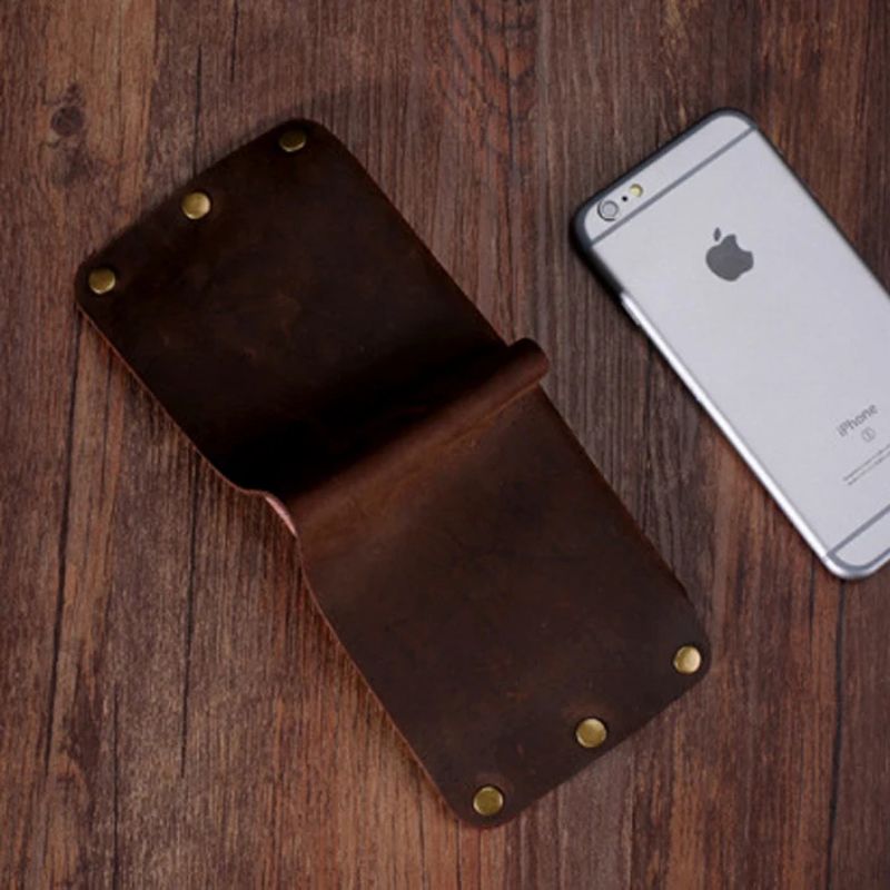 Coffee brown leather wallet next to a smartphone on a wooden table, top view.