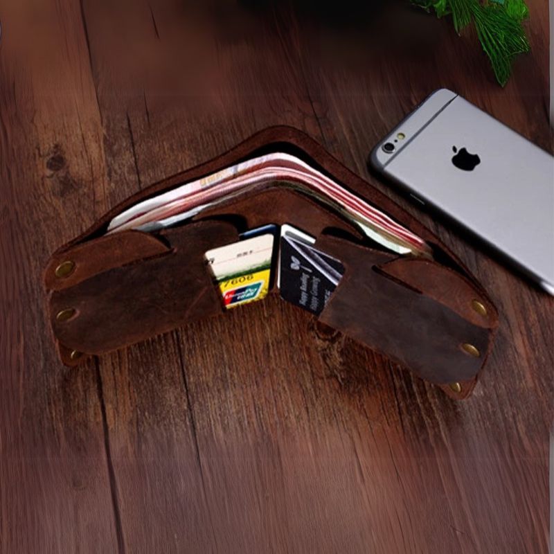 A coffee brown leather wallet with several cards and cash, next to a smartphone on a wooden surface.