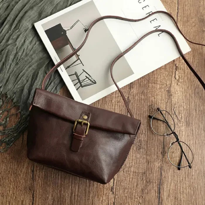 Coffee brown leather crossbody bag with elegant buckle and long strap, top view.