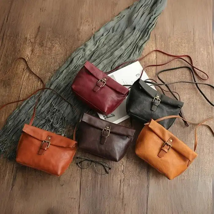 A set of leather crossbody bags in different colors on a wooden surface, top view.