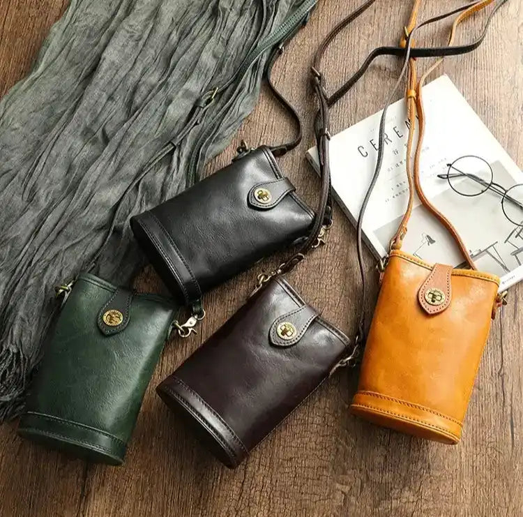 four leather crossbody bags in different colors arranged on a wooden table with accessories.