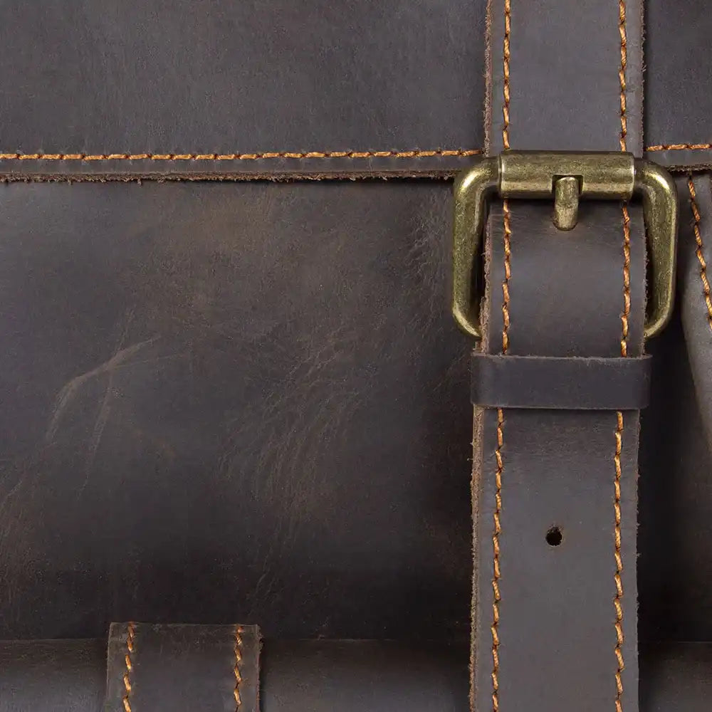 Detailed view of a leather bag with brass hardware and orange stitching.