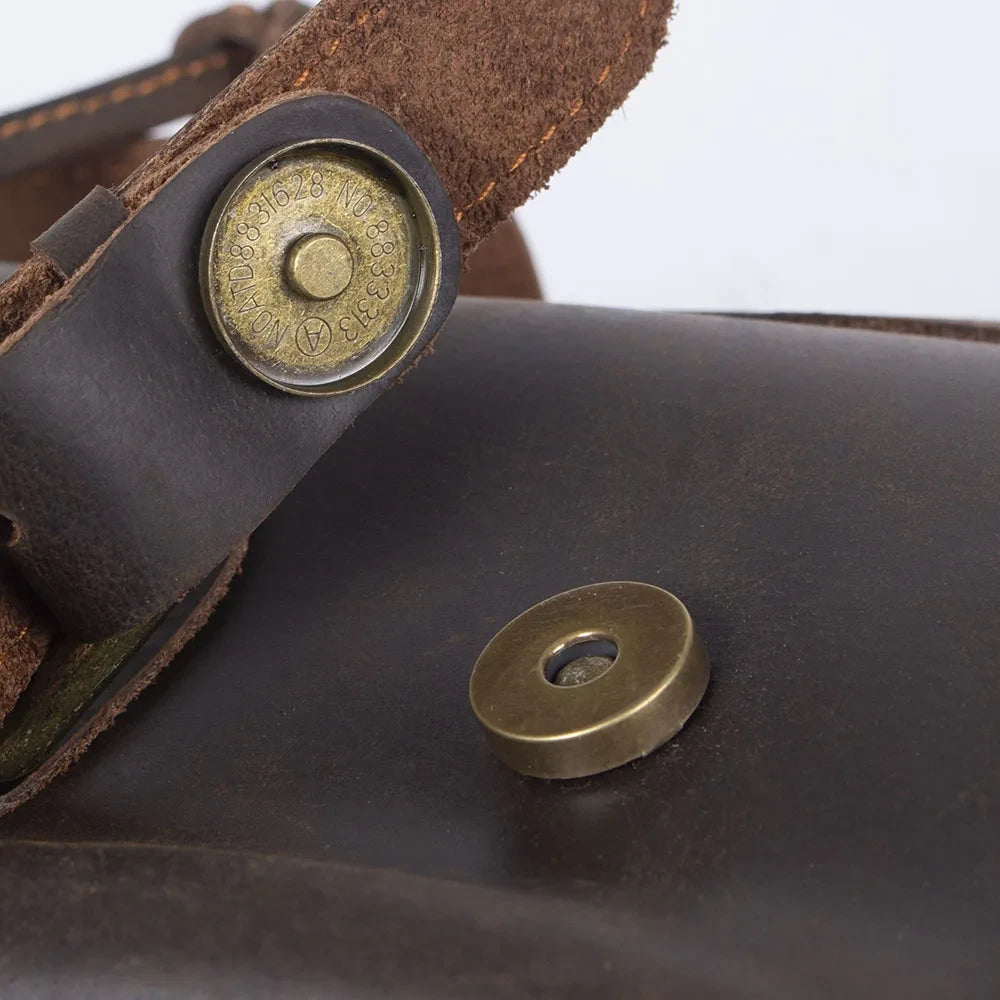 Close-up of a leather bag clasp with brass button and rivet.