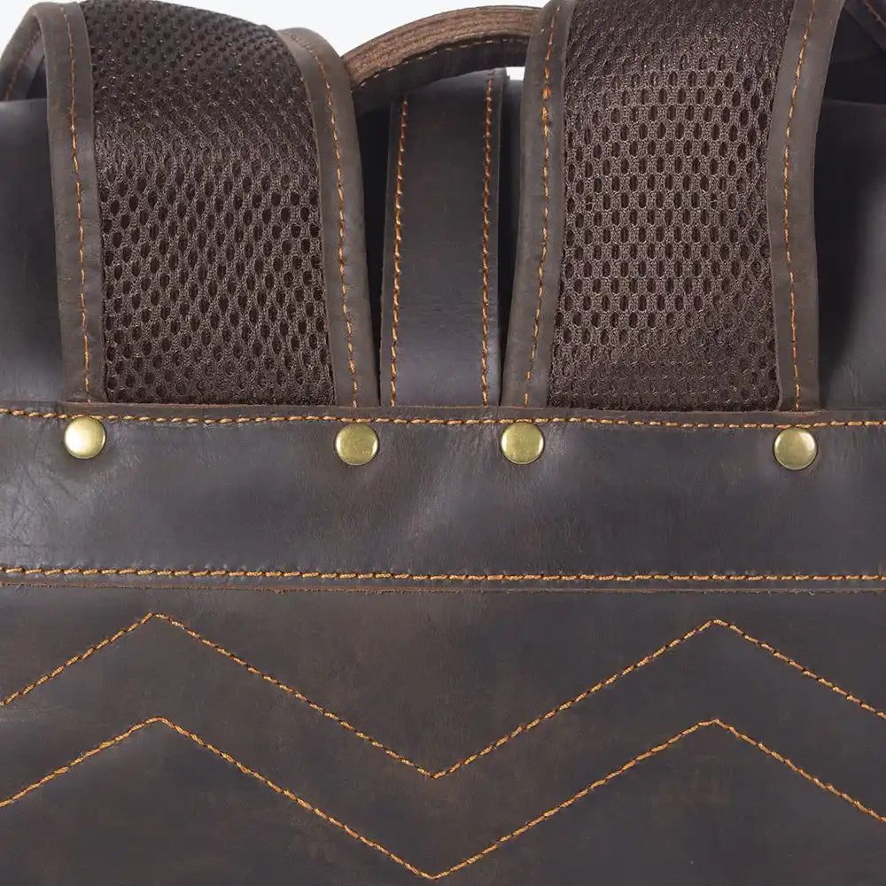 Detailed image showcasing the stitching, metal studs and mesh straps of a brown leather bag.